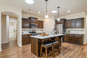 Kitchen with backsplash, arched walkways, dark brown cabinetry, decorative light fixtures, and appliances with stainless steel finishes
