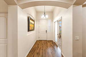 Entryway with a chandelier, wood finished floors, and arched walkways