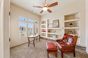 Living area with built in shelves, carpet, and ceiling fan