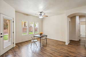 Dining area featuring a textured ceiling, arched walkways, dark wood-style flooring, and a ceiling fan