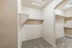 Spacious closet featuring light colored carpet, attic access, and arched walkways