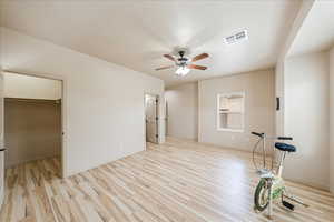 Unfurnished bedroom featuring light wood-style flooring, a spacious closet, and a ceiling fan