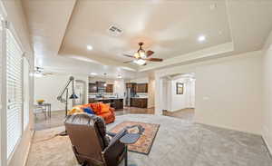 Living room featuring arched walkways, a tray ceiling, light colored carpet, and recessed lighting