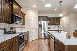 Kitchen with dark brown cabinets, appliances with stainless steel finishes, decorative backsplash, and recessed lighting