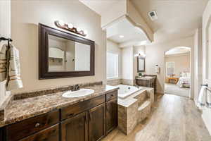 Ensuite bathroom featuring two vanities, a bath, and light wood finished floors