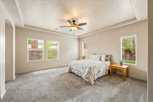 Bedroom featuring a tray ceiling, light carpet, a textured ceiling, a ceiling fan, and arched walkways