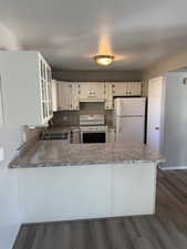 Kitchen featuring white appliances, dark wood-style flooring, white cabinetry, a peninsula, and glass insert cabinets