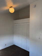 Bedroom featuring a textured ceiling, dark carpet, and a closet