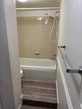 Full bathroom with dark wood-type flooring,  shower combination, and a textured ceiling