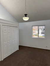 Bedroom featuring a textured ceiling, vaulted ceiling, dark carpet, and a closet