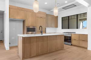 Kitchen featuring pendant lighting, appliances with stainless steel finishes, light wood-type flooring, an island with sink, and recessed lighting