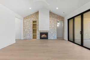 Unfurnished living room featuring light wood-style floors, a stone fireplace, built in features, high vaulted ceiling, and recessed lighting