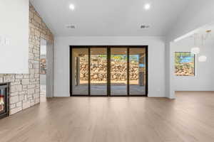 Unfurnished living room featuring plenty of natural light, light wood-type flooring, a stone fireplace, recessed lighting, and high vaulted ceiling