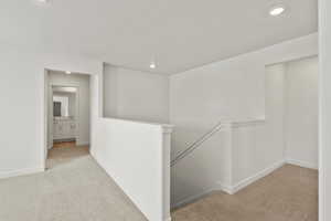 Corridor featuring light carpet, an upstairs landing, and recessed lighting