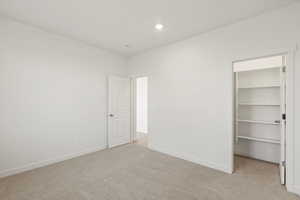 Unfurnished bedroom with a spacious closet, light carpet, and recessed lighting