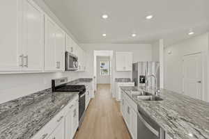 **DISCLAIMER, exterior and interior option may vary**Kitchen with appliances with stainless steel finishes, light stone countertops, light wood-style floors, white cabinetry, and recessed lighting