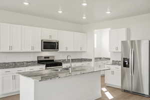 **DISCLAIMER, exterior and interior option may vary**Kitchen with appliances with stainless steel finishes, light stone countertops, white cabinets, light wood-type flooring, and recessed lighting