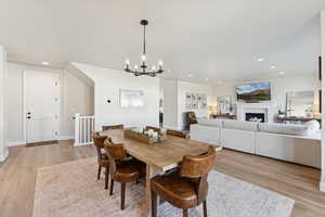 Dining area with light wood-style floors, recessed lighting, a lit fireplace, and a chandelier
