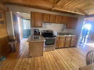 Kitchen featuring a wooden ceiling with exposed beams, stainless steel electric range, brown cabinetry, light countertops, and light wood-style floors
