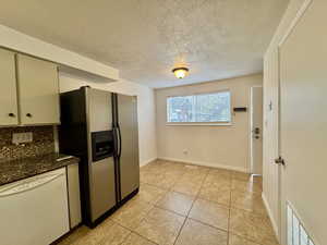 Kitchen featuring white dishwasher, stainless steel fridge with ice dispenser, decorative backsplash, light tile patterned floors, and a textured ceiling