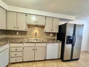 Kitchen featuring stainless steel fridge with ice dispenser, white dishwasher, decorative backsplash, a textured ceiling, and light tile patterned floors