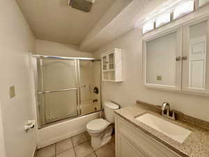 Bathroom with a textured ceiling, shower / bath combination with glass door, light tile patterned floors, and vanity