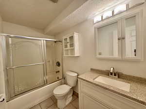 Full bathroom with a textured ceiling, light tile patterned floors, combined bath / shower with glass door, and vanity