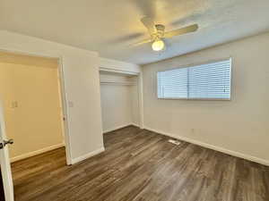Unfurnished bedroom with a textured ceiling, dark wood finished floors, ceiling fan, and a closet