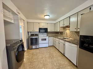Kitchen featuring white appliances, backsplash, dark countertops, light tile patterned flooring, and a textured ceiling