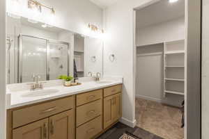 Full bath featuring double vanity, a shower stall, dark carpet, and a spacious closet