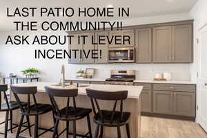 Kitchen with gray cabinetry, backsplash, a breakfast bar area, and a kitchen island with sink