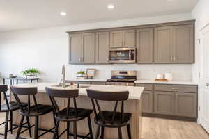 Kitchen featuring gray cabinetry, tasteful backsplash, a kitchen bar, appliances with stainless steel finishes, and recessed lighting