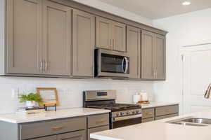 Kitchen featuring gray cabinetry, stainless steel appliances, light stone counters, backsplash, and recessed lighting