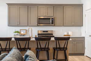 Kitchen featuring gray cabinets, tasteful backsplash, stainless steel appliances, light stone counters, and a breakfast bar