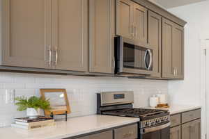 Kitchen with gray cabinets, appliances with stainless steel finishes, decorative backsplash, and light stone counters
