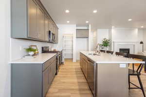 Kitchen with a kitchen breakfast bar, stainless steel appliances, gray cabinetry, a kitchen island with sink, and light stone counters