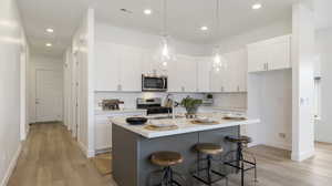 Kitchen with decorative backsplash, a center island with sink, white cabinets, hanging light fixtures, and a breakfast bar