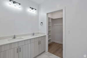 Full bathroom with double vanity, a spacious closet, and light marble finish floors