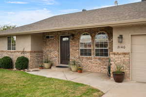 View of exterior entry featuring covered porch, brick siding, and stucco siding