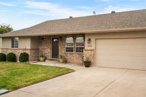 Single story home featuring brick siding, a shingled roof, driveway, a front yard, and stucco siding
