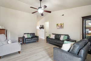 Living room with vaulted ceiling, light wood finished floors, and a ceiling fan