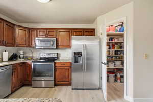 Kitchen with appliances with stainless steel finishes, light wood-style floors, light stone countertops, and brown cabinets