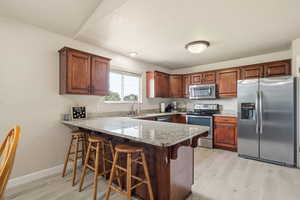 Kitchen with appliances with stainless steel finishes, a breakfast bar area, a peninsula, and light wood-style floors