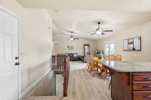 Kitchen featuring vaulted ceiling, light wood-style flooring, light stone countertops, ceiling fan, and a breakfast bar