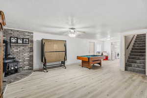 Playroom featuring light wood-style flooring, billiards table, a wood stove, a textured ceiling, and ceiling fan