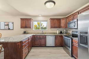 Kitchen featuring stainless steel appliances, a peninsula, light wood finished floors, and light stone countertops