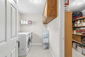 Washroom with a textured ceiling, washing machine and dryer, light colored carpet, and cabinet space