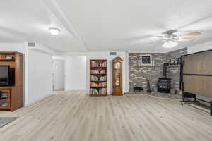 Unfurnished living room with a textured ceiling, a wood stove, light wood-style floors, ceiling fan, and brick wall