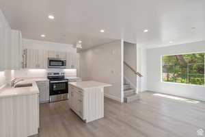 Kitchen with a center island, appliances with stainless steel finishes, recessed lighting, light wood finished floors, and light stone counters