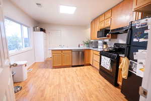 Kitchen featuring a peninsula, black appliances, light countertops, light wood finished floors, and under cabinet range hood